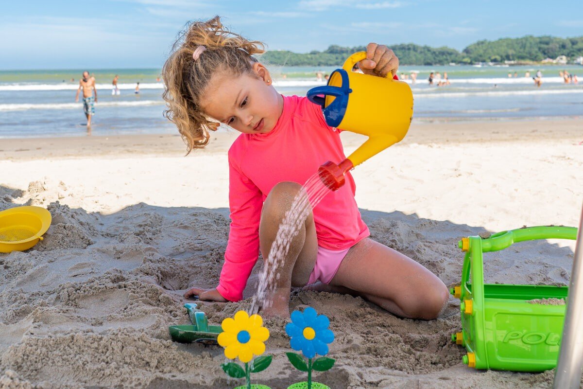 menina brincando com regador de brinquedo na praia