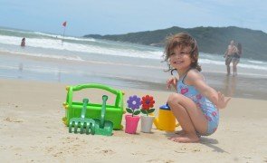 menina brincando com balde e plantas na praia