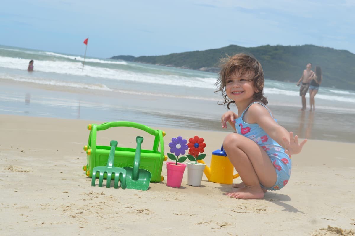 menina brincando com balde e plantas na praia